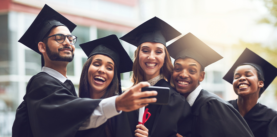 Group of happy international graduates wearing caps and gowns, taking a selfie while celebrating their academic achievement and graduation success.